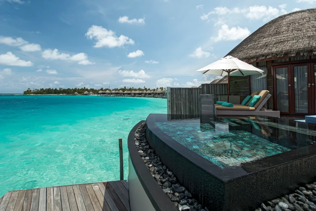 Water Villa du Constance Halaveli Maldives avec piscine privée sur pilotis, vue sur lagon turquoise et ciel ensoleillé.