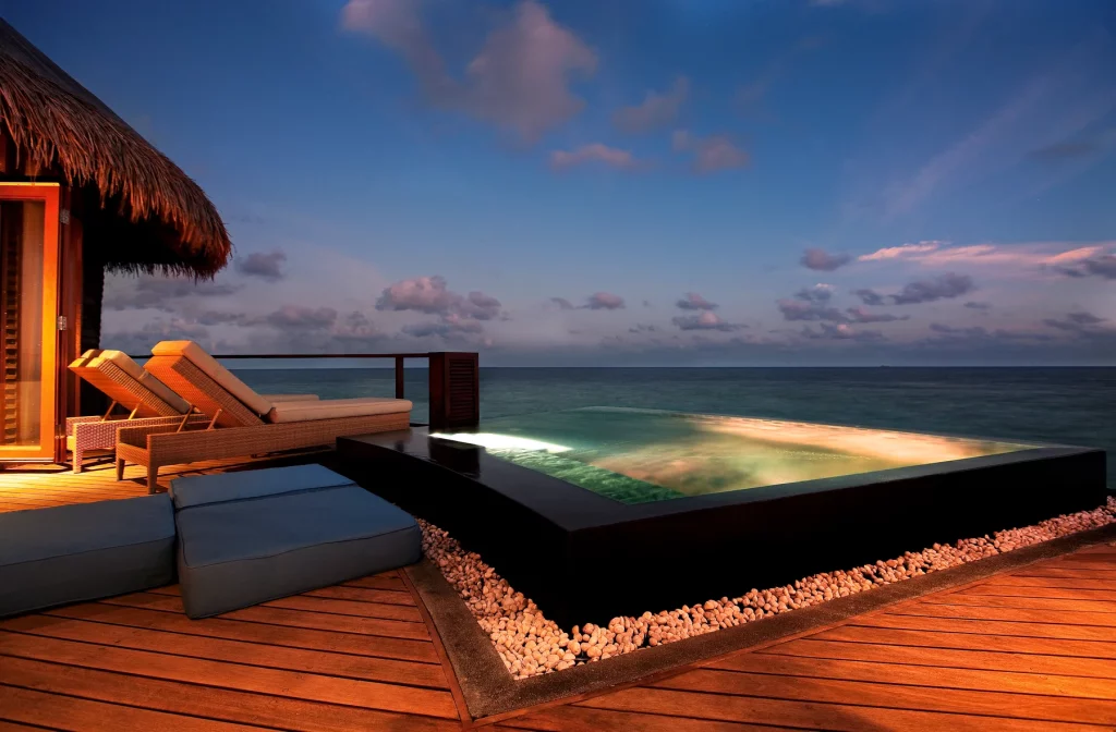Water Villa du Constance Halaveli Maldives illuminée la nuit avec piscine privée et reflet sur le lagon calme