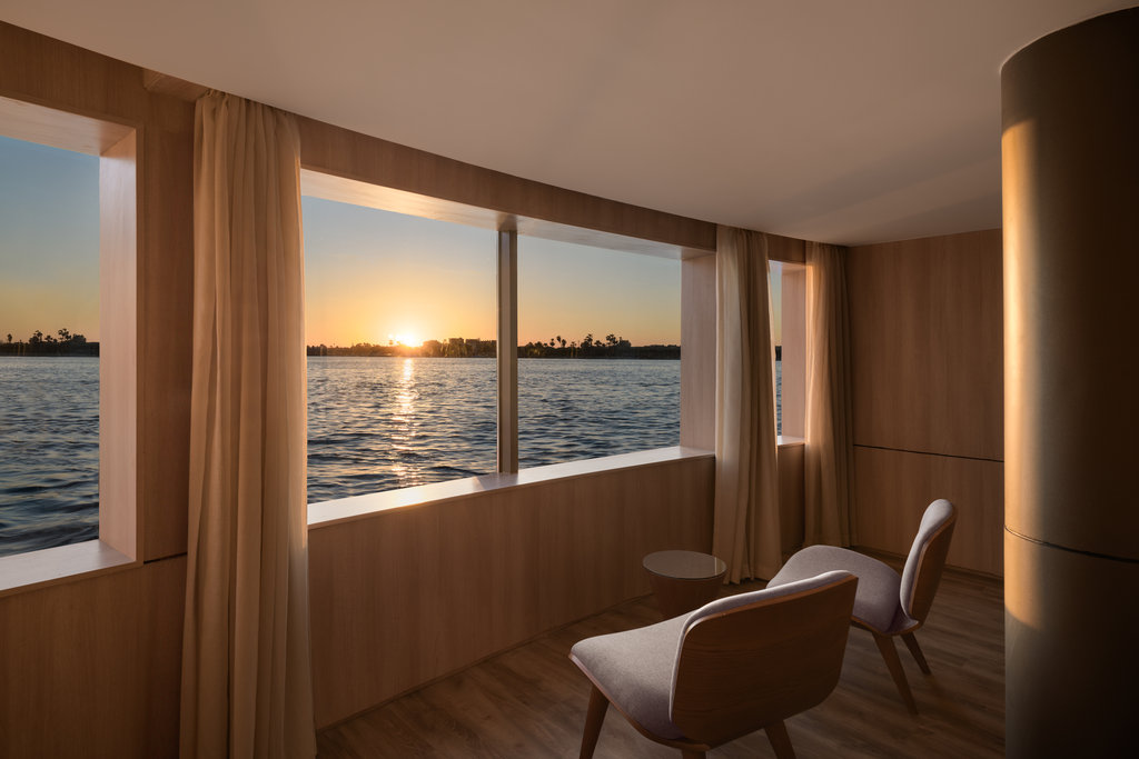 Balcon intérieur de la Suite Polaris du Storia the Dahabeya, avec large baie vitrée sur le Nil au coucher du soleil, croisière de luxe en Égypte