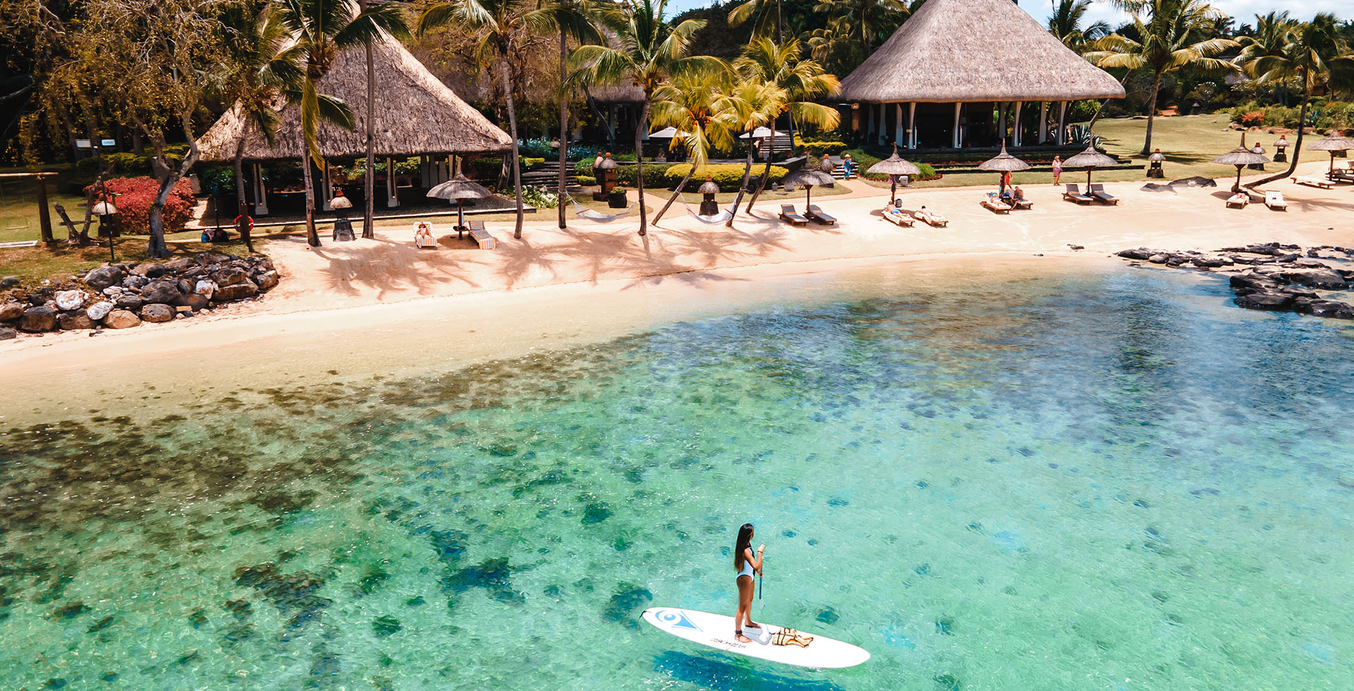 Activités nautiques au The Oberoi Beach Resort Mauritius, paddle sur lagon turquoise face à la plage et aux pavillons tropicaux.