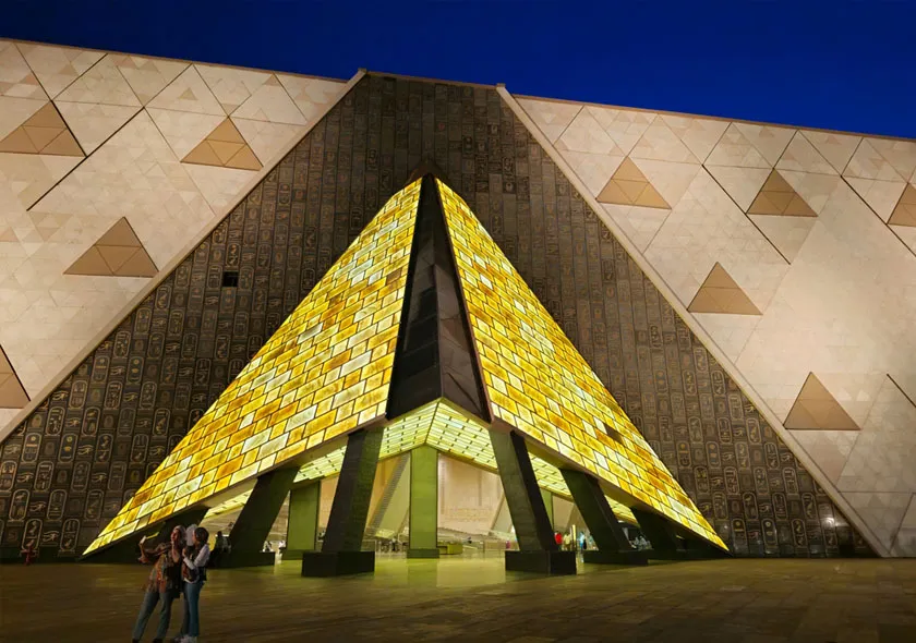 Entrée illuminée en forme de pyramide du Grand Egyptian Museum au Caire, architecture moderne inspirée de l’Égypte antique.