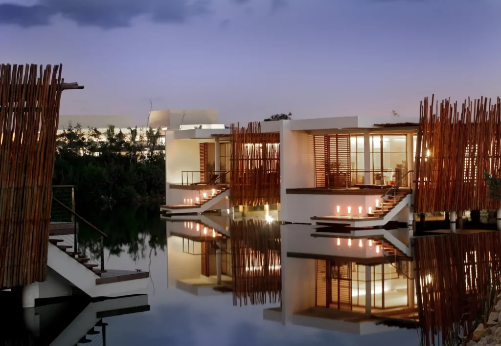 Deluxe Overwater Lagoon Suite du Rosewood Mayakoba au crépuscule, suites illuminées se reflétant dans le lagon émeraude entouré de bambous, Riviera Maya Mexique
